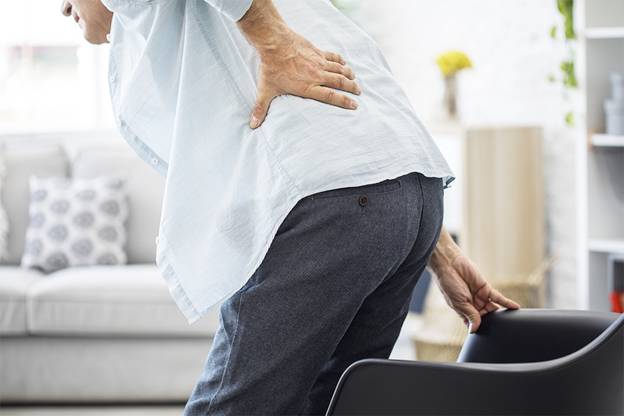 腰の痛みで腰に手を当てる白いシャツの男性